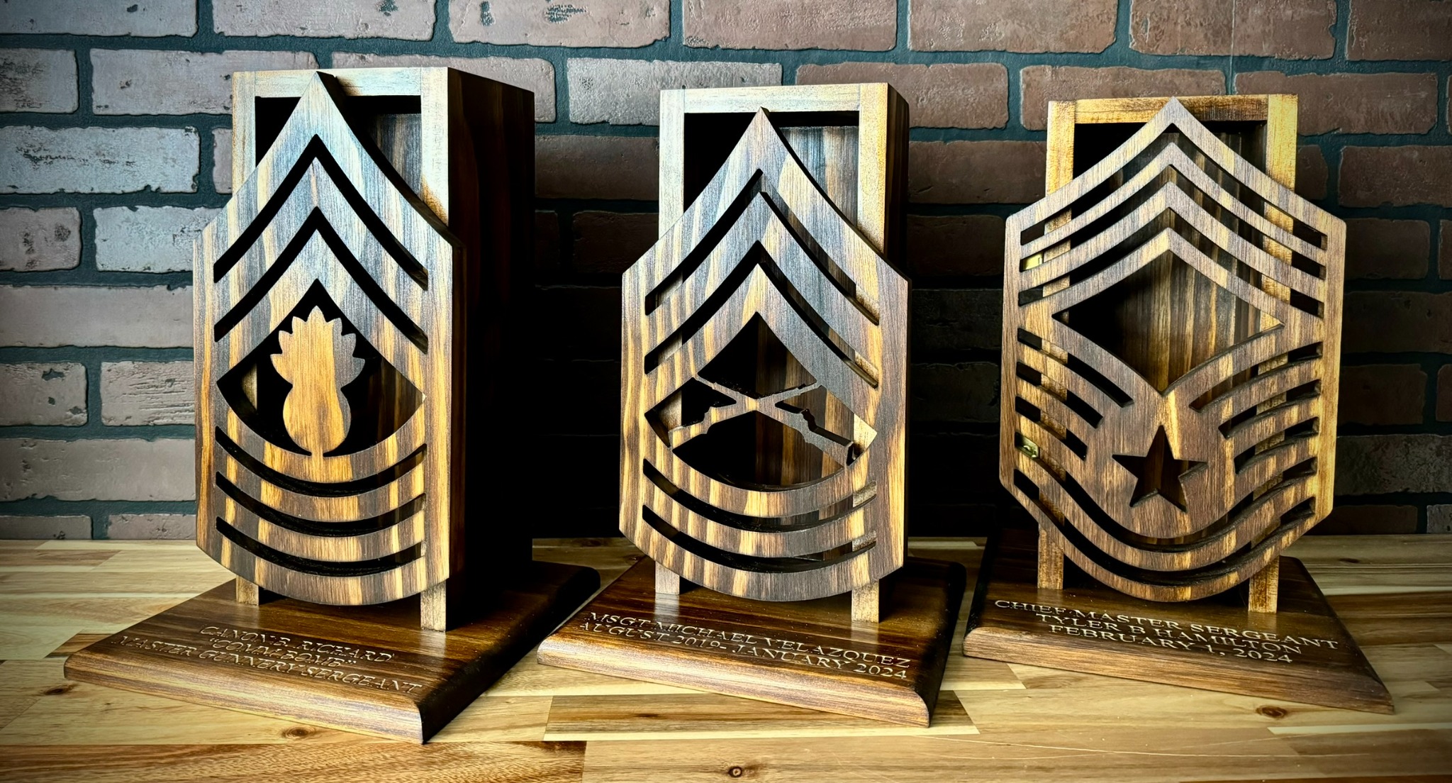 Three custom wooden military rank cases displayed on a wood table against a brick wall